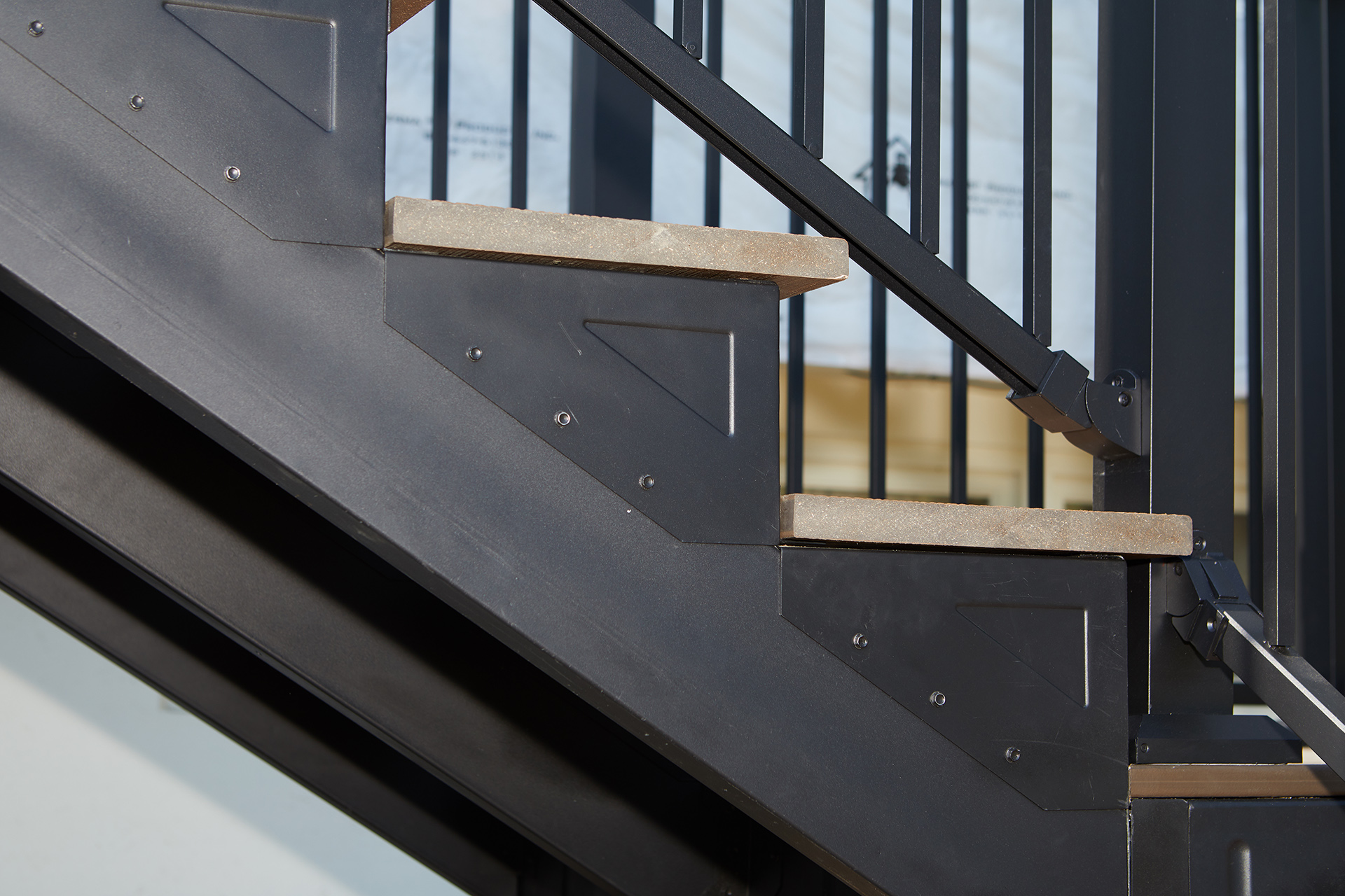 Close-up of steel stair framing, installed with a lighter tone step and black railing.
