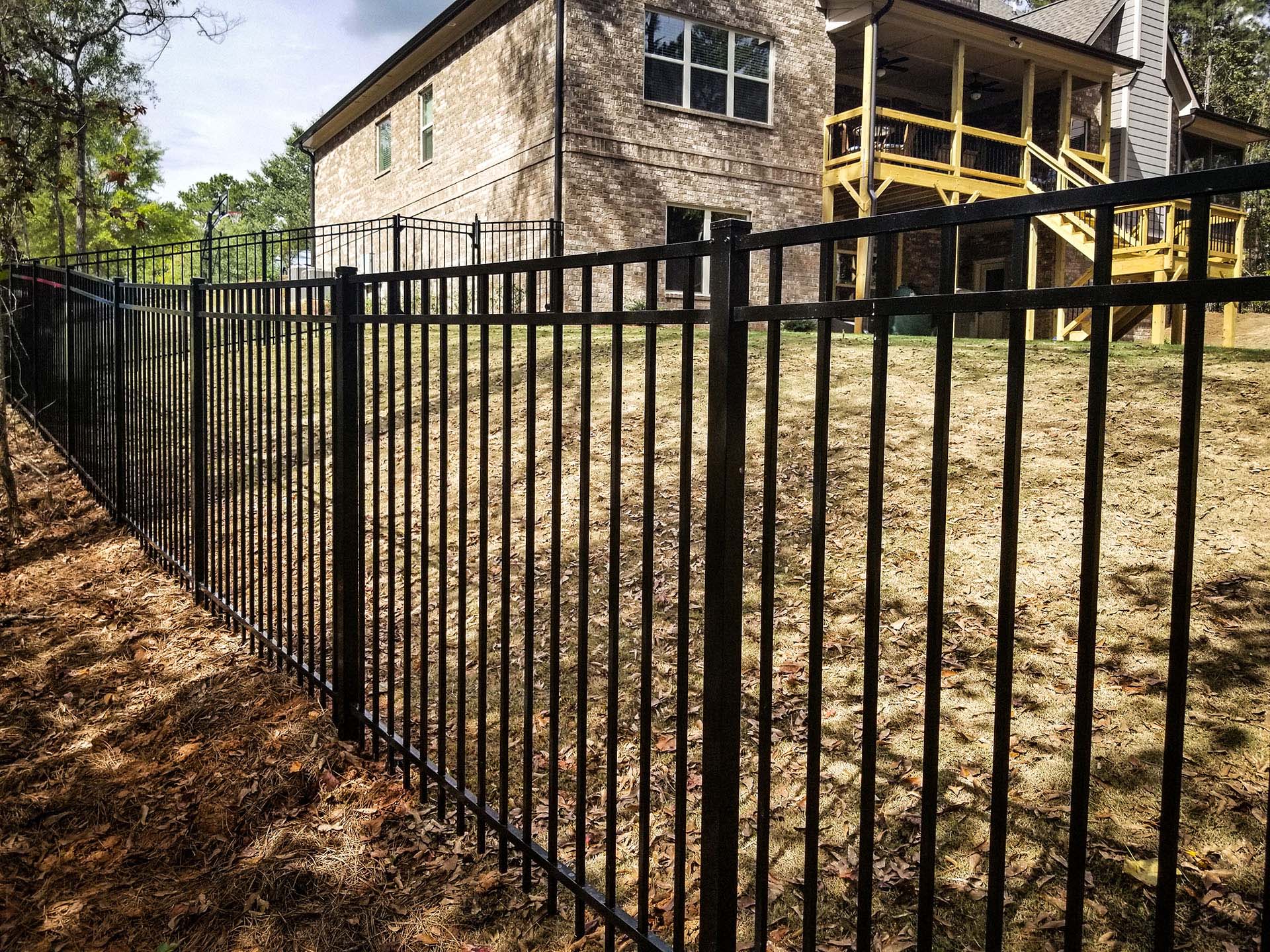 Side-view of black aluminum fencing meeting a brick home to enclose the backyard