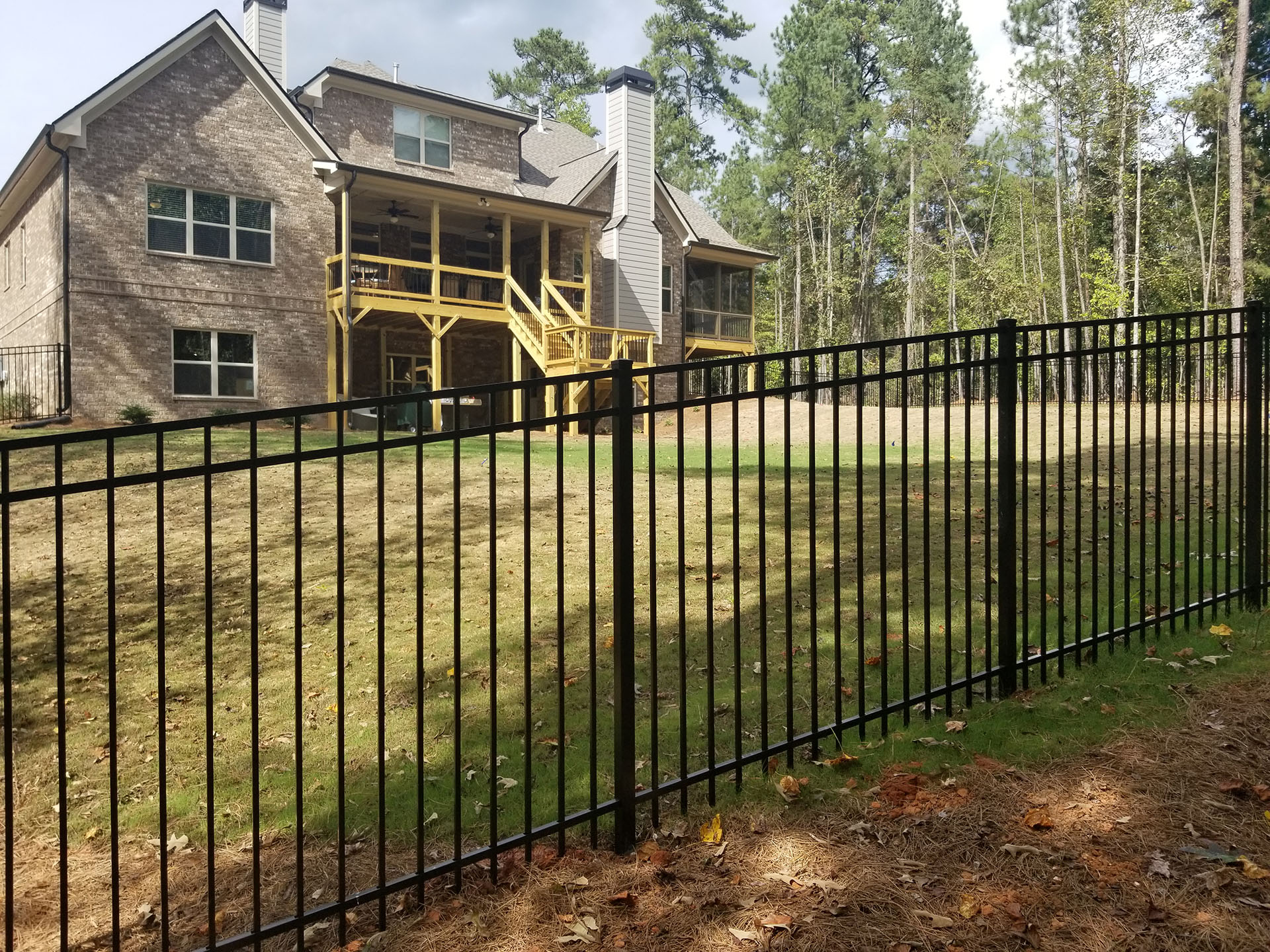 Black aluminum fencing enclosing a brick home with yellow porch.