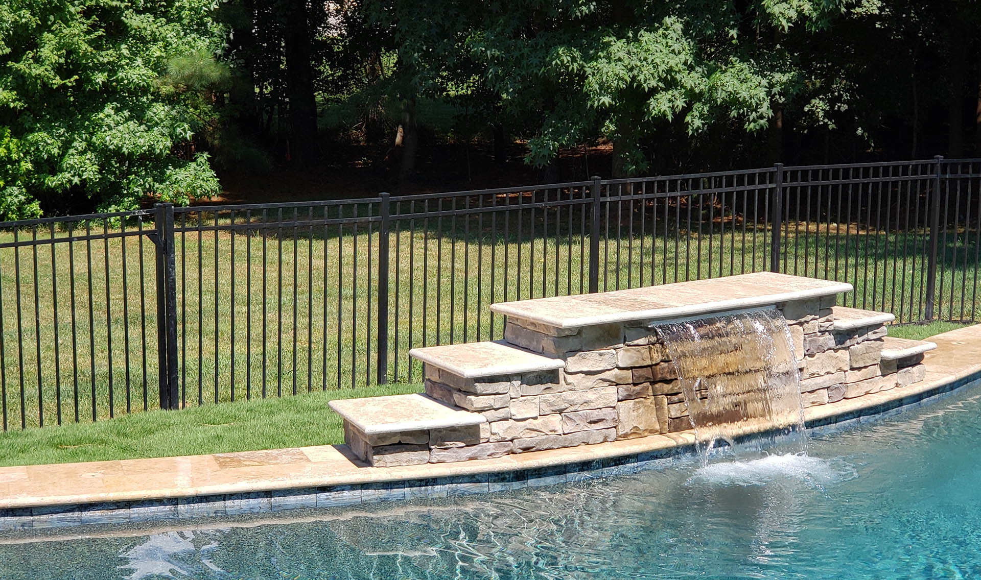 Black aluminum fencing behind a waterfall feature in a swimming pool.