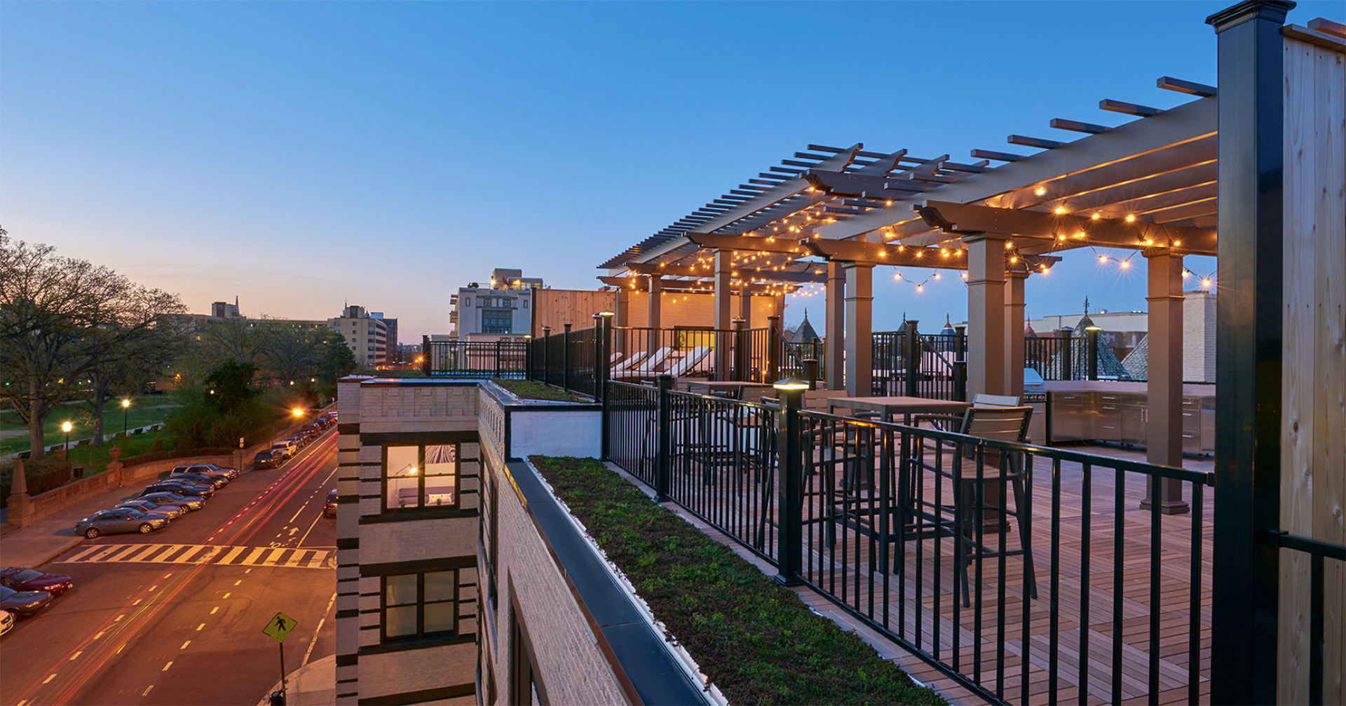 Evening view of a rooftop deck with pergola and LED-lit railings overlooking a city street