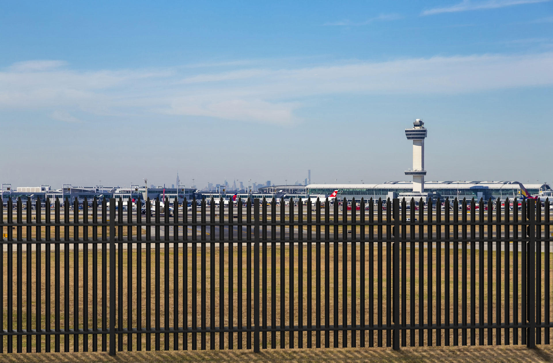 Durable high-security steel fencing at an airport, safeguarding against unauthorized access with a view of the control tower. 