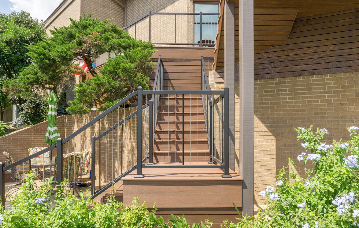 Multi-level deck stairs with vertical cable railing leading down to an outdoor entertainment area.