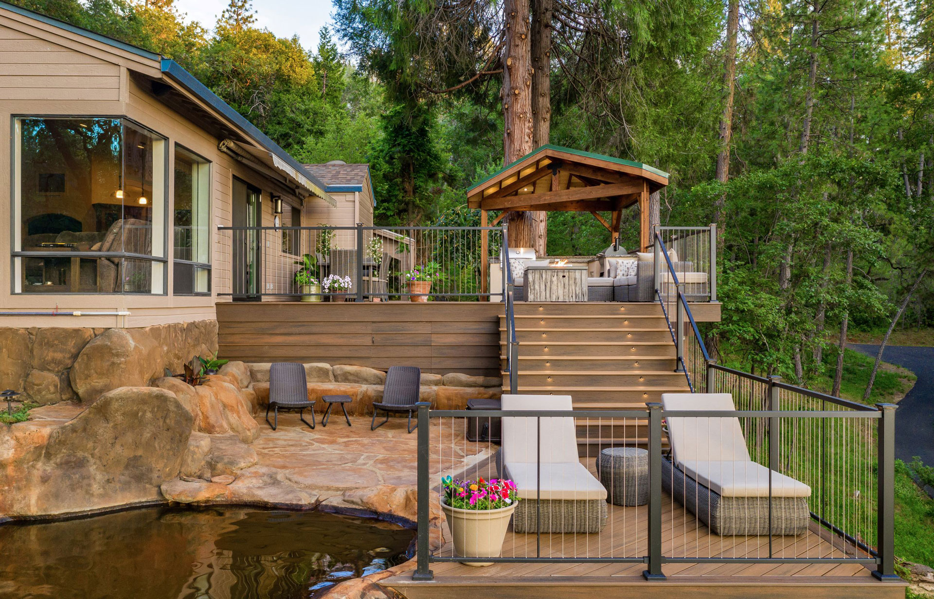 Cable railing enclosing  a multi-level deck with patio furniture and a rock swimming pool.