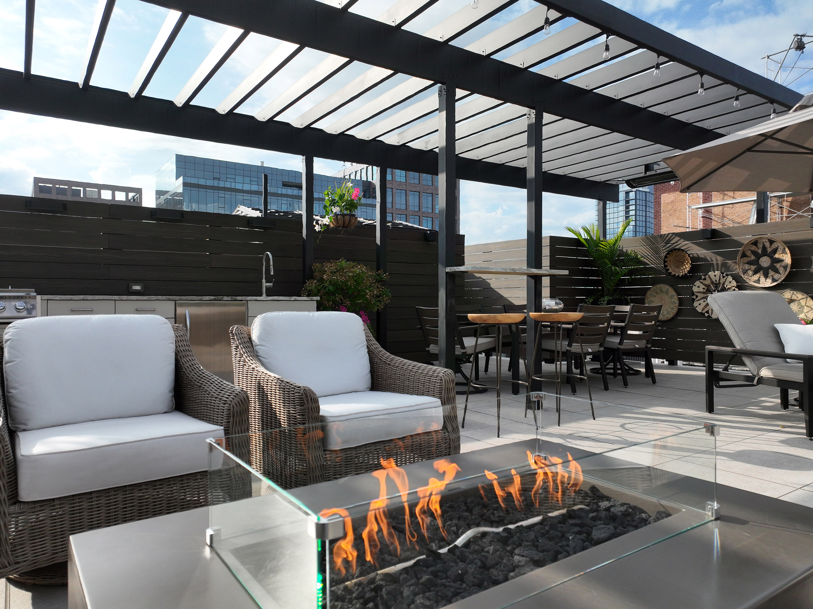 Outdoor steel pergola over a rooftop deck space with a fireplace and white chairs.