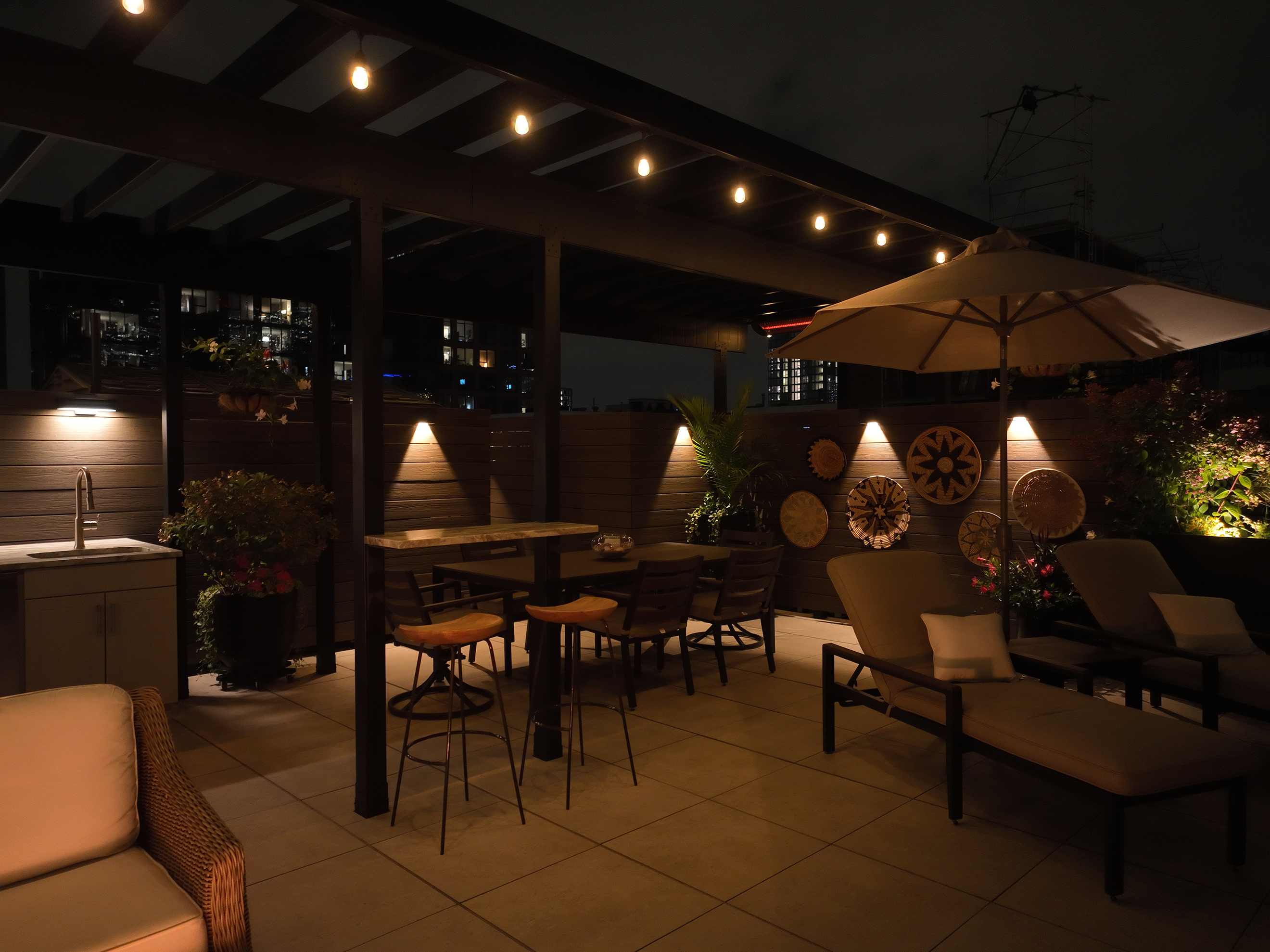 Steel pergola with string lights over outdoor living space with lounge chairs and tables.